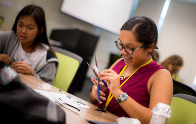 A high school student smiling while cutting paper and working on an experiment in a pre-college program.