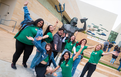 A group of UC San Diego students smiling with their hands in the air in front of the Triton statue